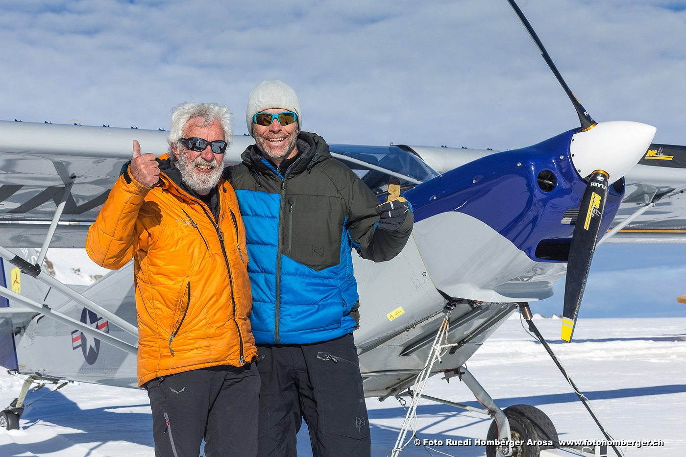Zwei Männer vor einem Leichtflugzeug im Schnee, einer zeigt den Daumen nach oben