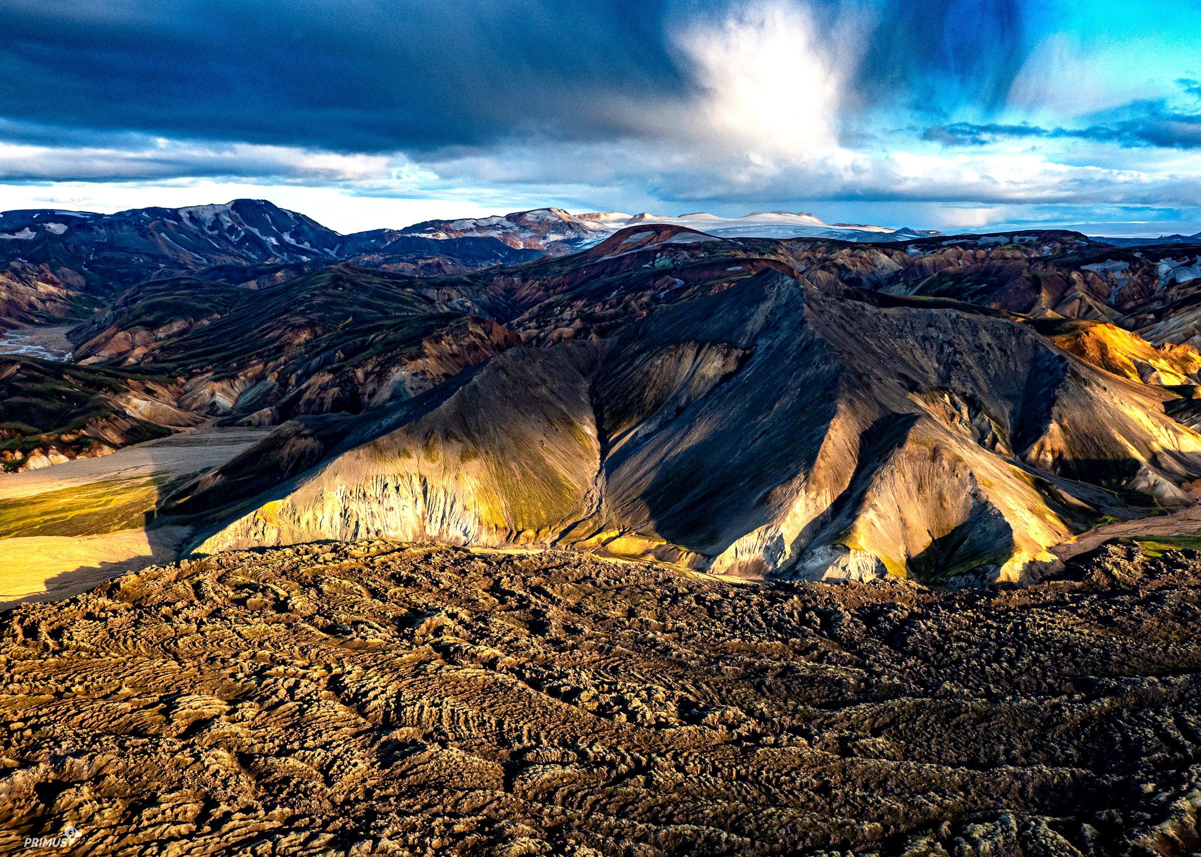 Luftaufnahme aus dem eigenen Flugzeug: farbige Berge und ein Lavafeld unter Gewitterwolken, Island