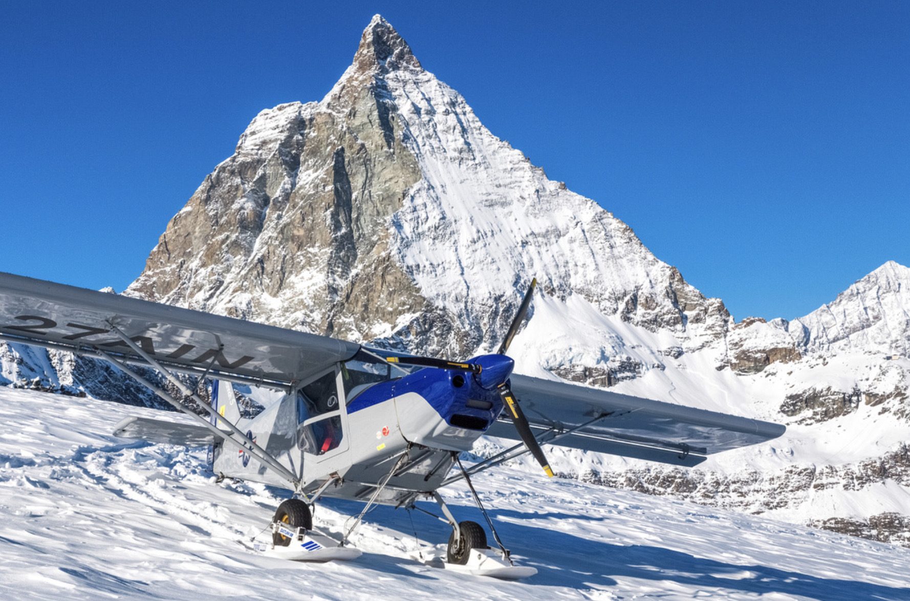 Leichtflugzeug auf Ski im Schnee vor einem steilen, verschneiten Gipfel