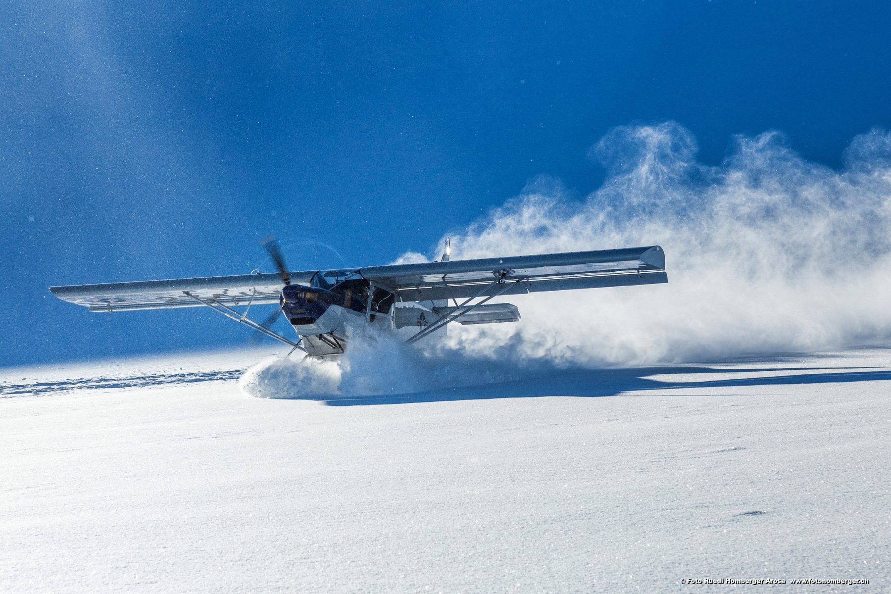 Leichtflugzeug auf Ski wirbelt eine grosse Pulverschneewolke auf