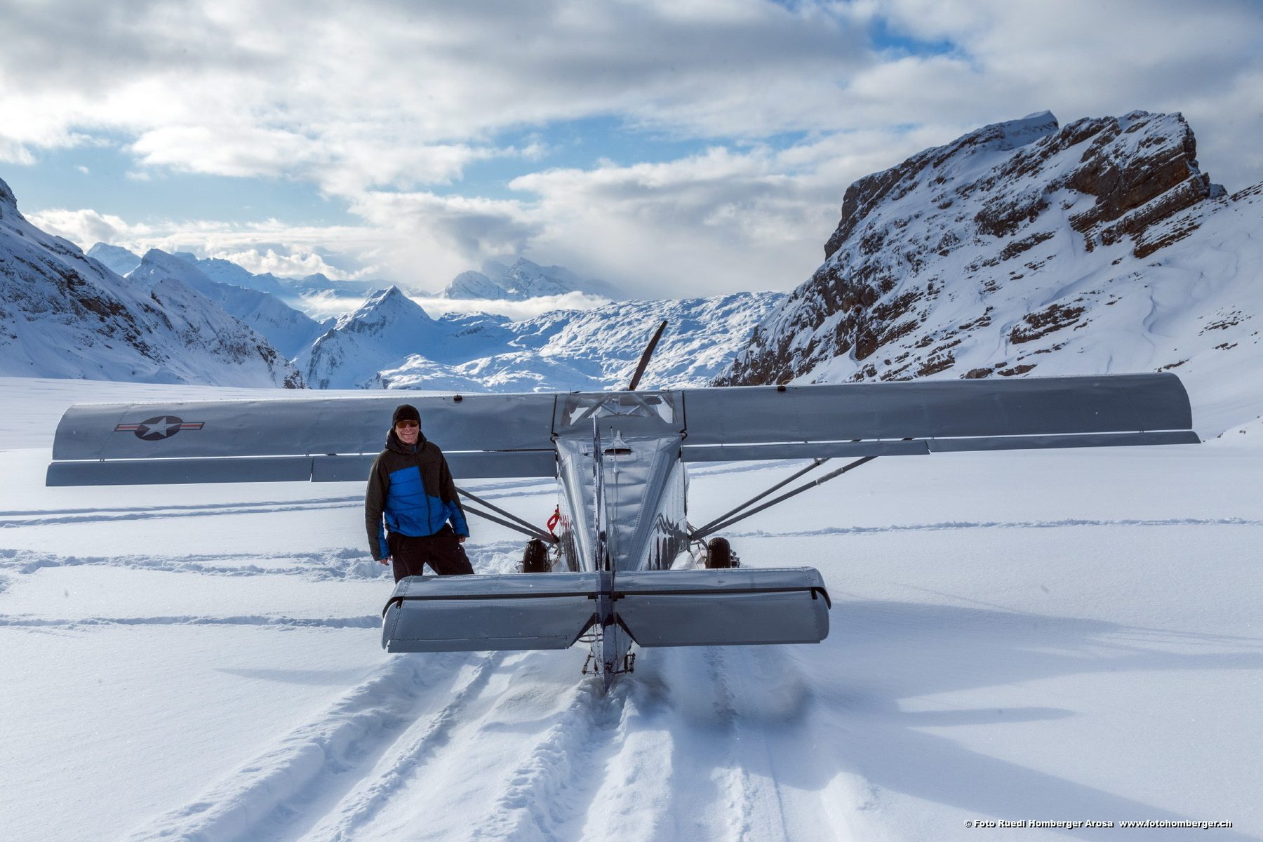 Person steht im Schnee neben einem Leichtflugzeug, dahinter Felsgipfel
