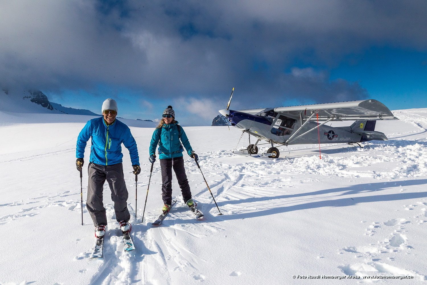 Zwei Personen auf Tourenski auf einem Gletscher, dahinter ein Leichtflugzeug