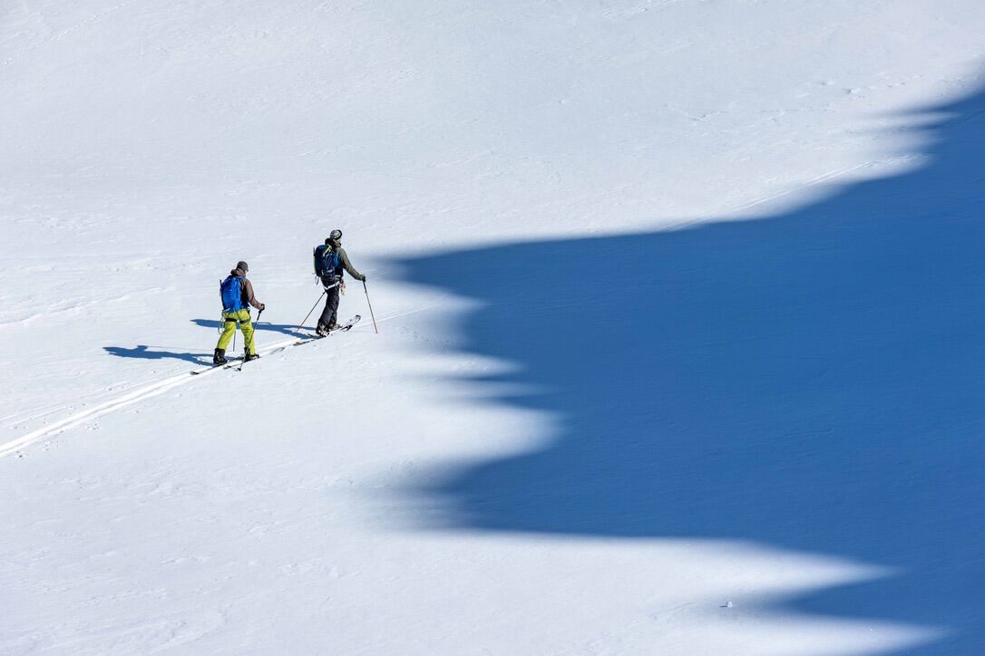 Zwei Personen auf Skitour steigen neben einem grossen Schatten über eine Schneeflanke
