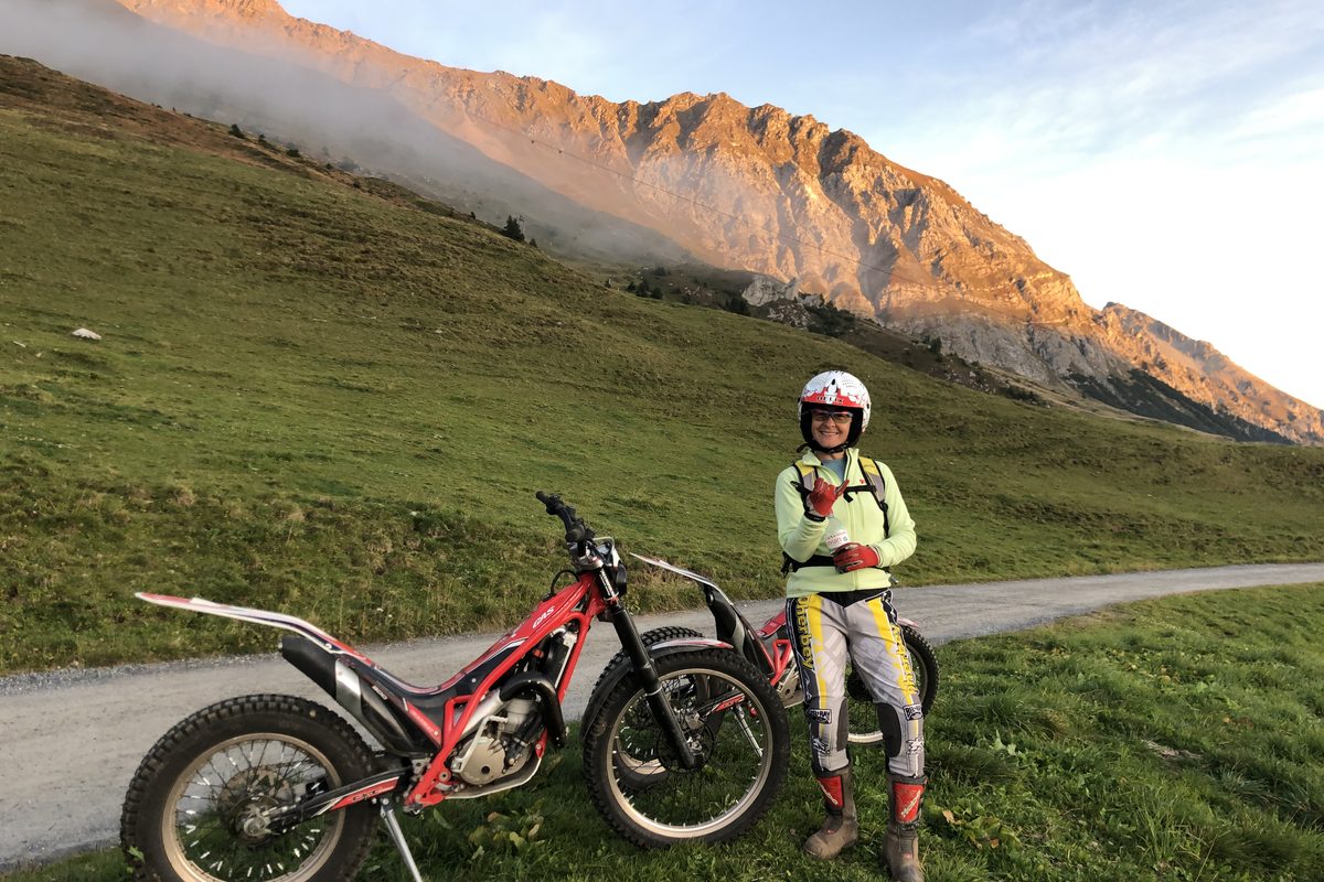 Person mit Helm neben einem Trial-Motorrad an einer Alpstrasse
